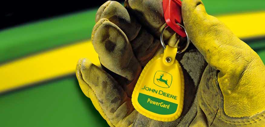 a gloved hand holding a John Deere PowerGard keychain